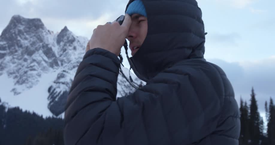 A man in a winter coat takes pictures of a mountain area