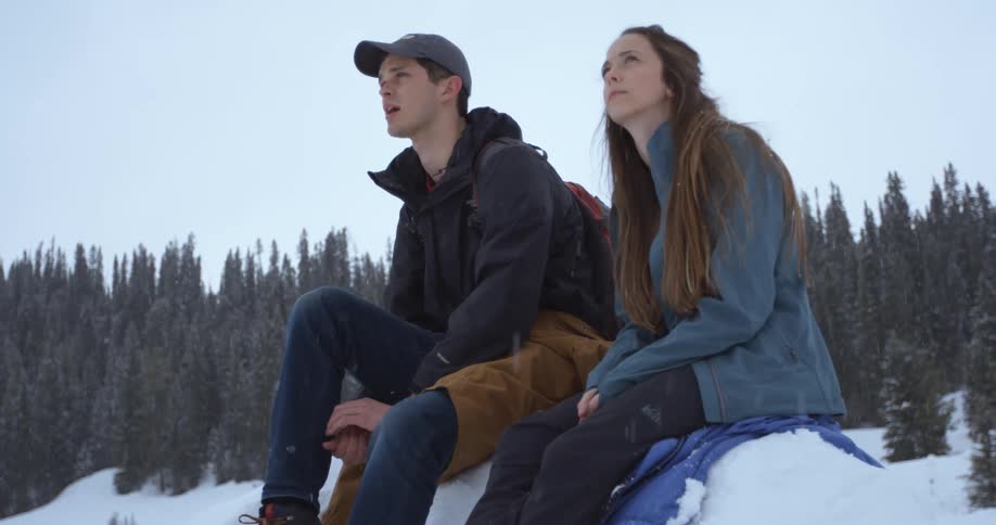 A man and woman sit on a snow pile and talk