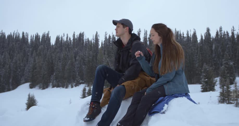 A man and woman sit outside in the snow on a snowy day