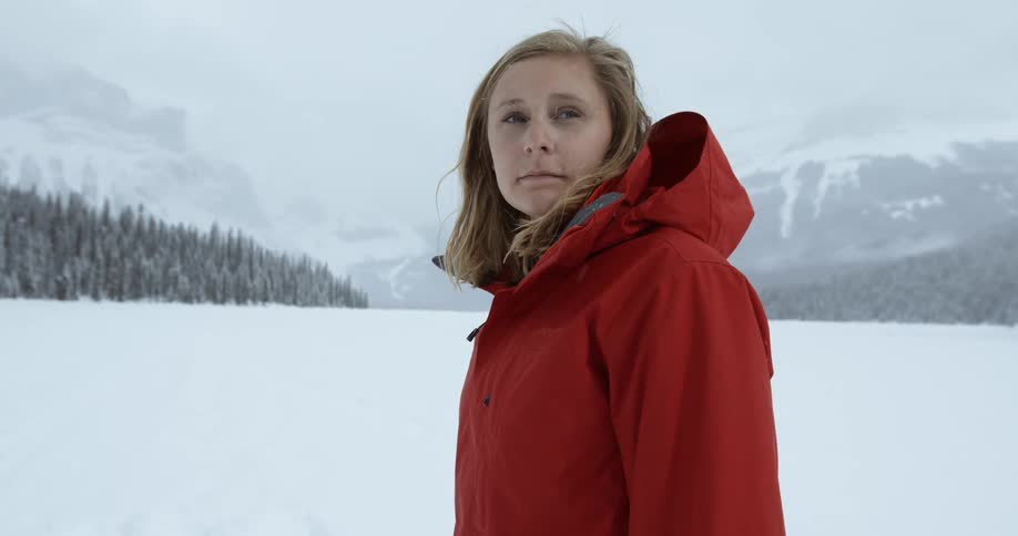A woman stands in an opening in the mountains during a snowstorm