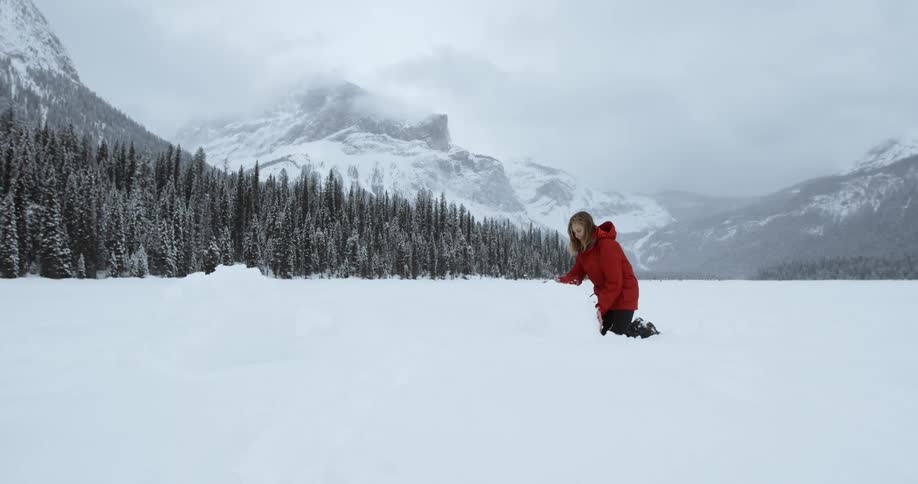 Woman on her knees rolling a ball to begin building a snowman