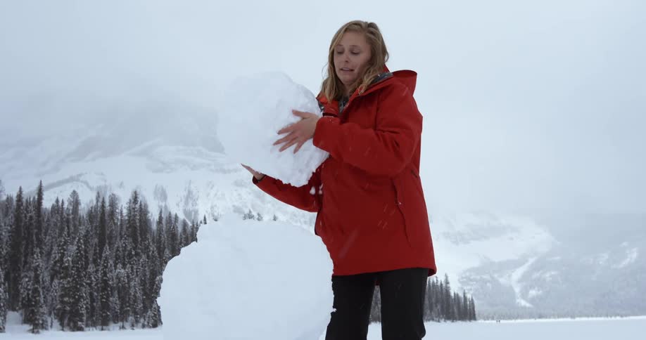 A woman is carrying a huge piece of snow for a snowman