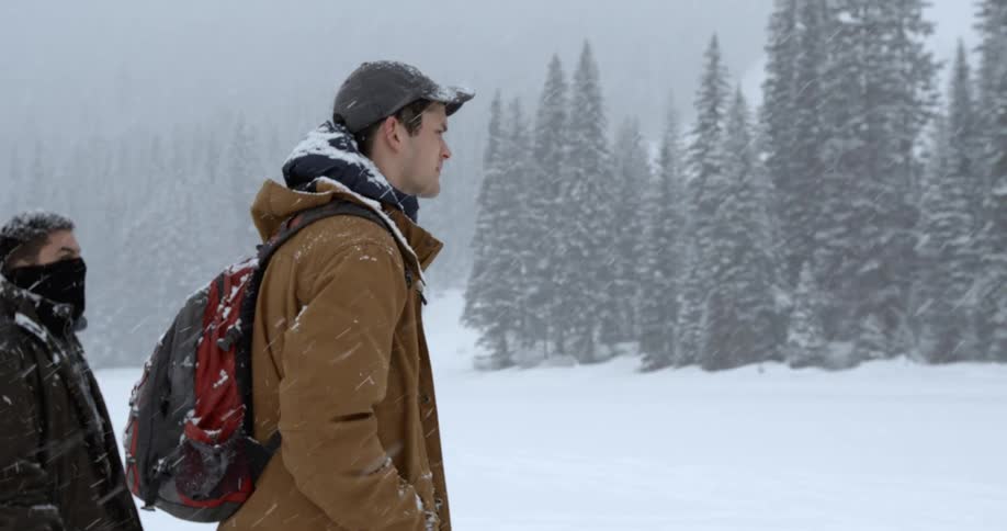 Two men walk through a field in the wilderness during a snowstorm