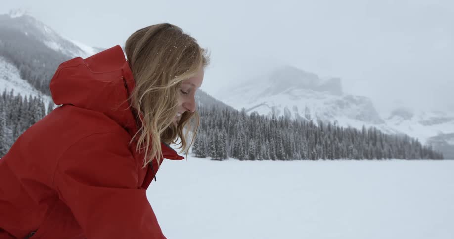 A woman building a snowman while it snows