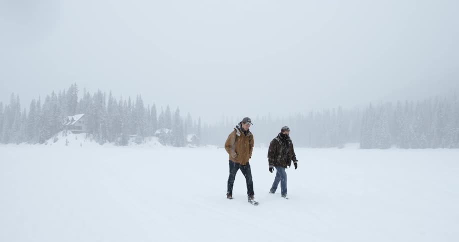 Two people are hiking over a field with heavy snow