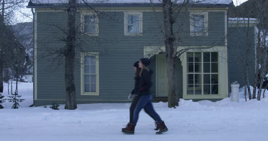 Two women walk in the snow past a house