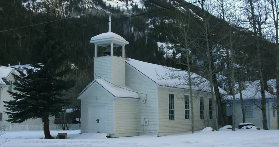A building has a small bell tower before a mountain behind it