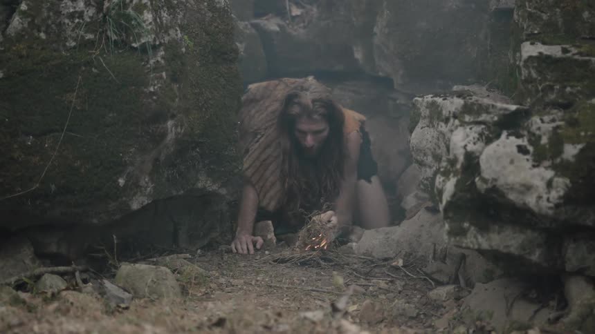 A cave man starts a fire with kindling