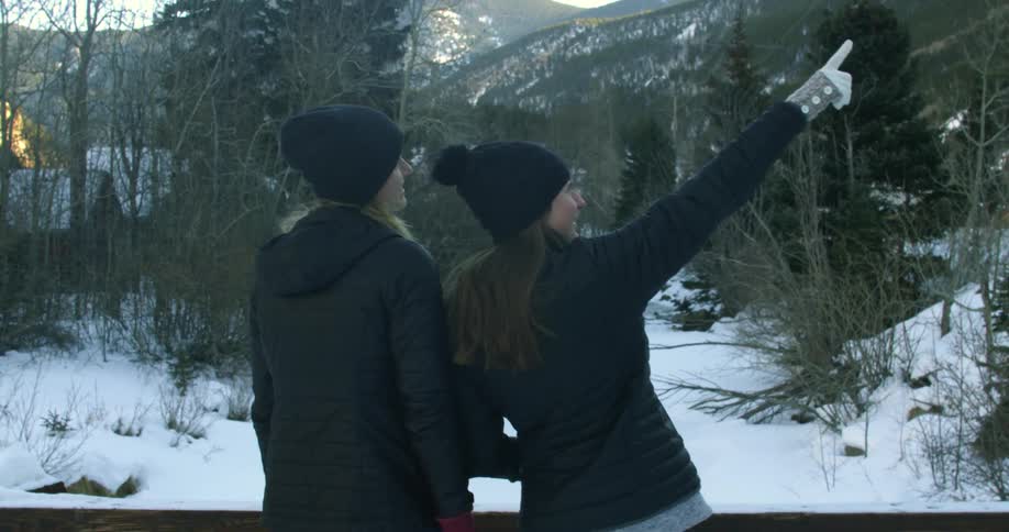 A woman pointing at something in a wintry landscape as another woman turns to look