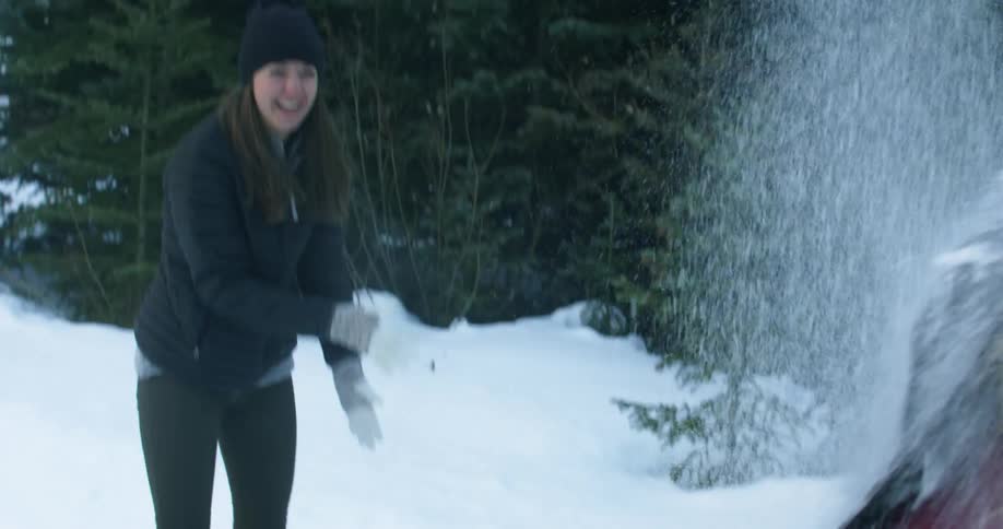 A woman laughs as she throws snow at another woman