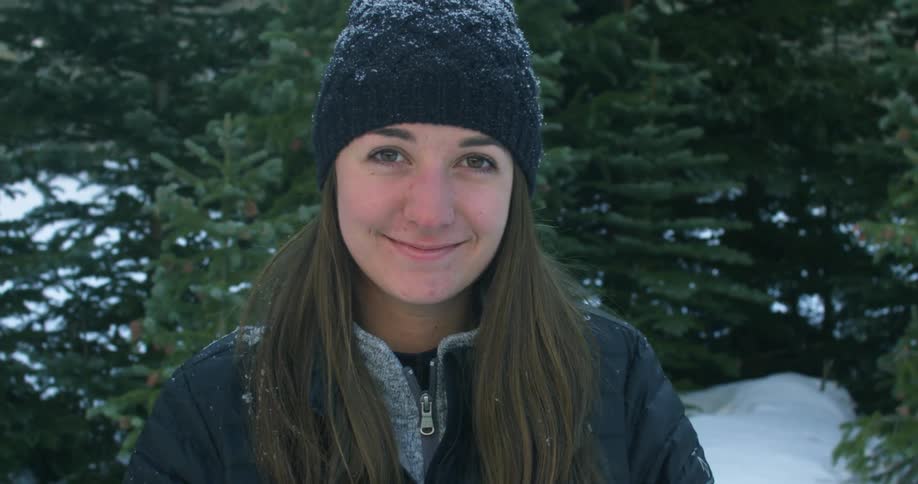 Woman standing outside by pine trees in the snow smiles