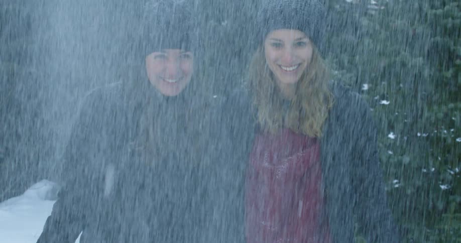 Two women smile as they throw snow in the air