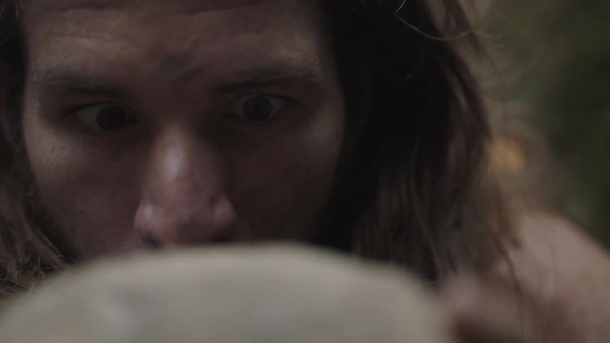 A man with crazy eyes is closely examining a rock