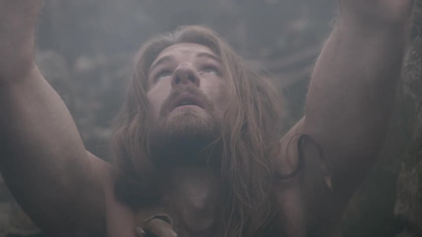 A man with long hair lifts a rock to the sky and down