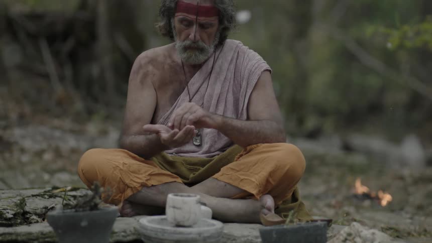 A man sits on the forest ground while snow begins to fall