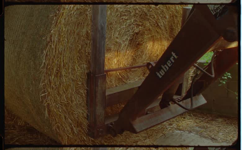 Rustylooking agricultural machine lifts a large bale of hay in the background is a green pasture