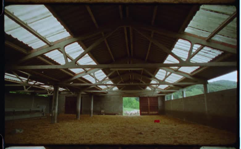 A barn located in the mountains is empty except for hay on the ground