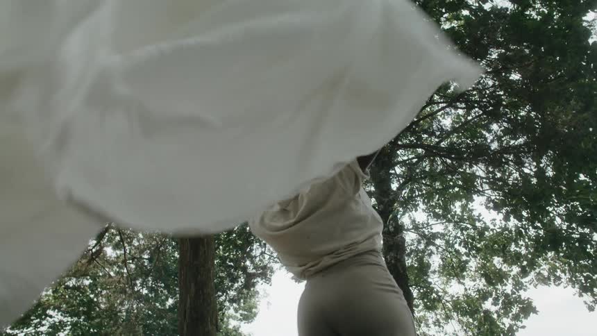 While outdoors a woman spins and turns white cloth in her hands