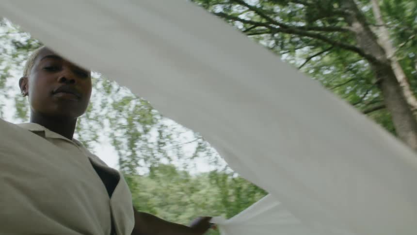 Woman with short hair and white shirt dances with white sheet in public park