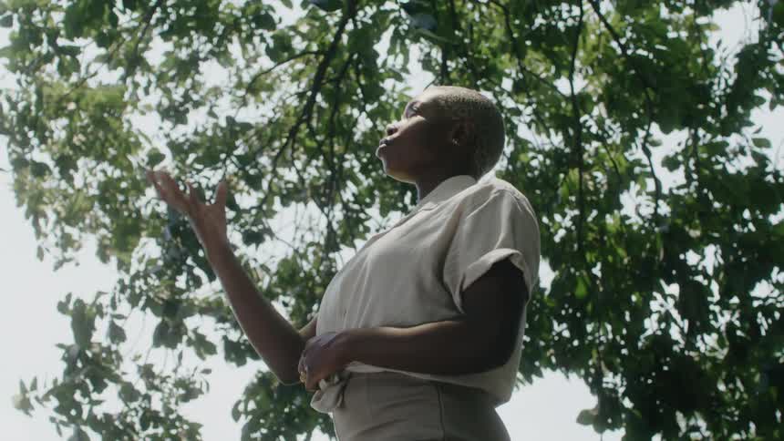 A woman is standing under a tree tossing an apple in the air
