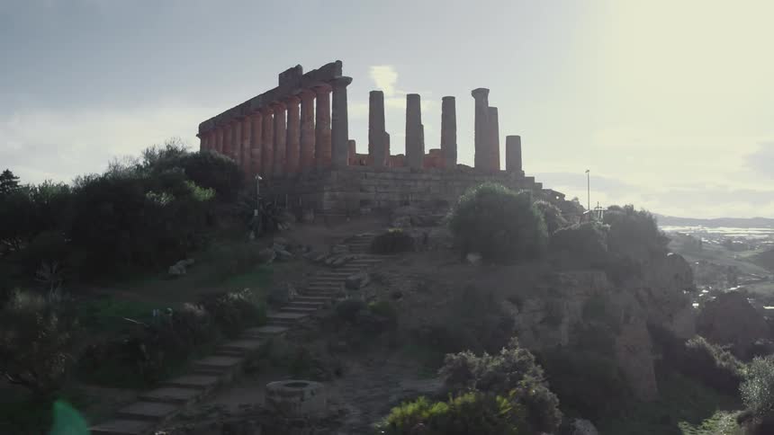 Greek ruins with tall columns stand high on a hillside in sunlight