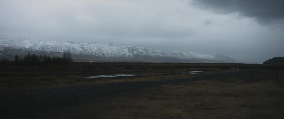 A barren field sits below a snow capped mountain range