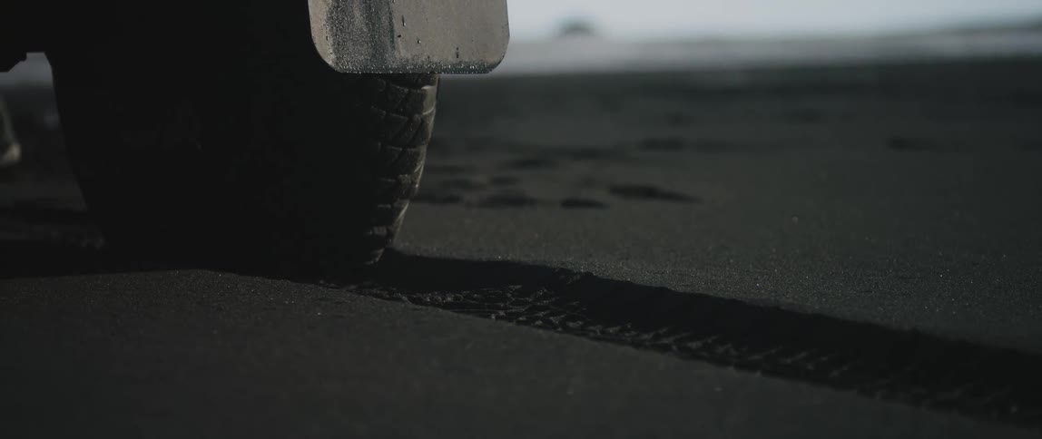 The tire tracks of a single tire on a vehicle is visible in the wet sand