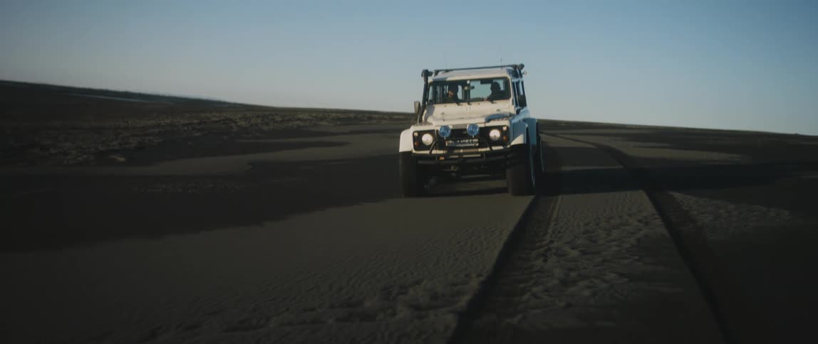 Two people drive a vehicle across a sandy landscape