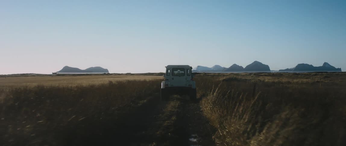 A vehicle travels along a dirt path through a grassland during the day