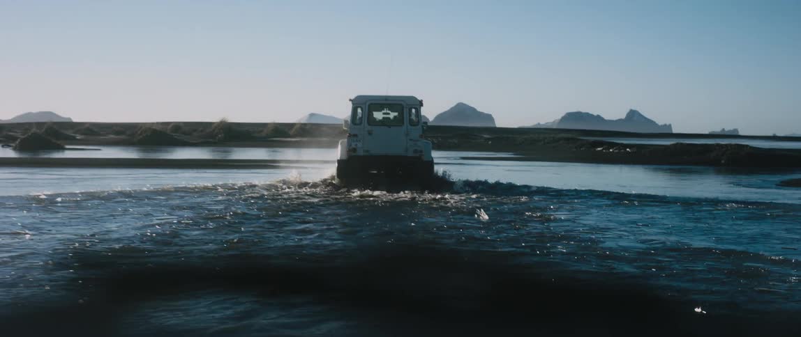 A car is driving through a pond of water at dusk