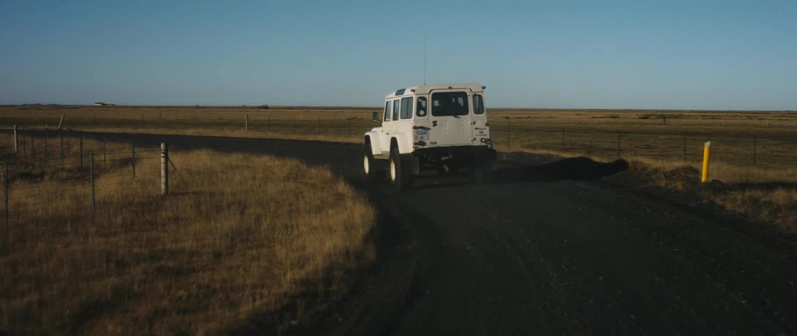 A white jeep drives along a curved dirt road that is in the middle of a large grass plain