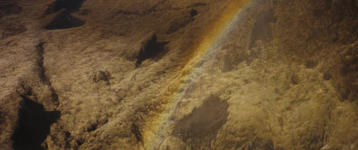 A rainbow over a river at the bottom of a slope in the wilderness during the day