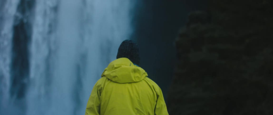 A person slowly crosses barren soil while walking towards a waterfall in the wilderness