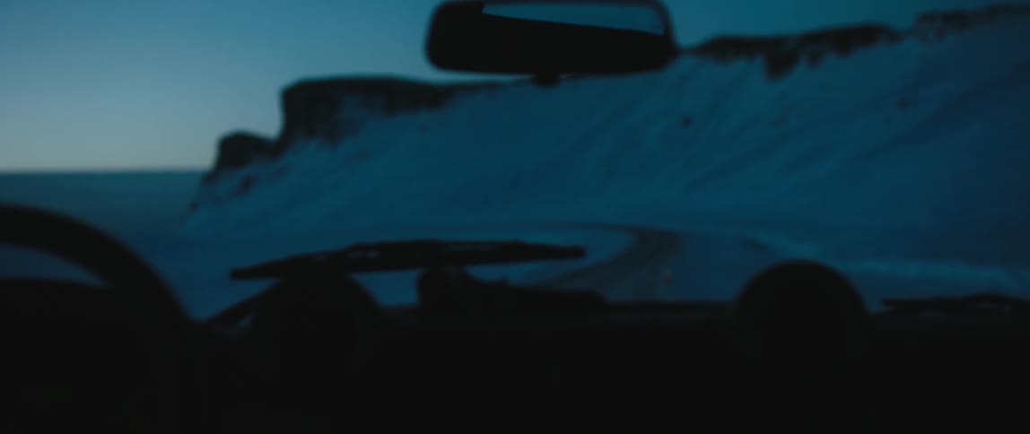 Vehicle traveling slowly on the snowy road next to the snow covered hills