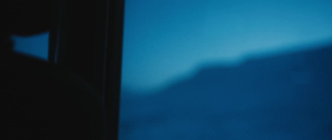 Jeep drives on snowy country road next to snowy field and mountain at dusk