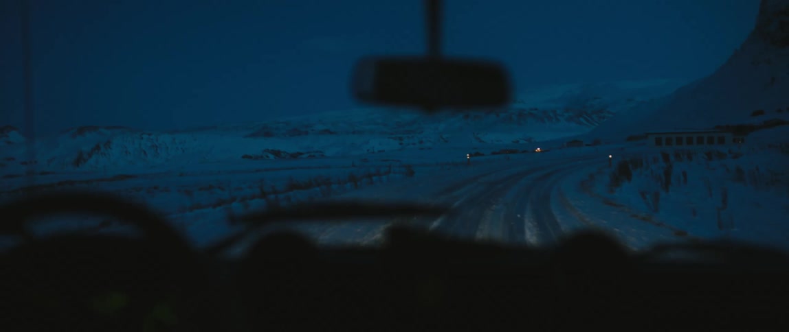 Jeep drives on snowy country road next to high mountain at night