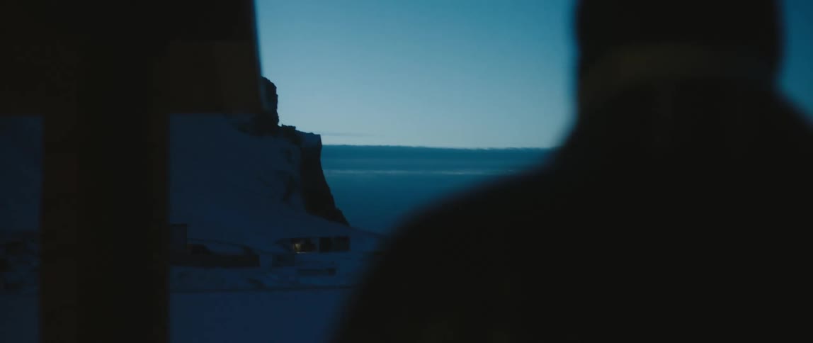 A man walks toward a shack below a cliff along the coast