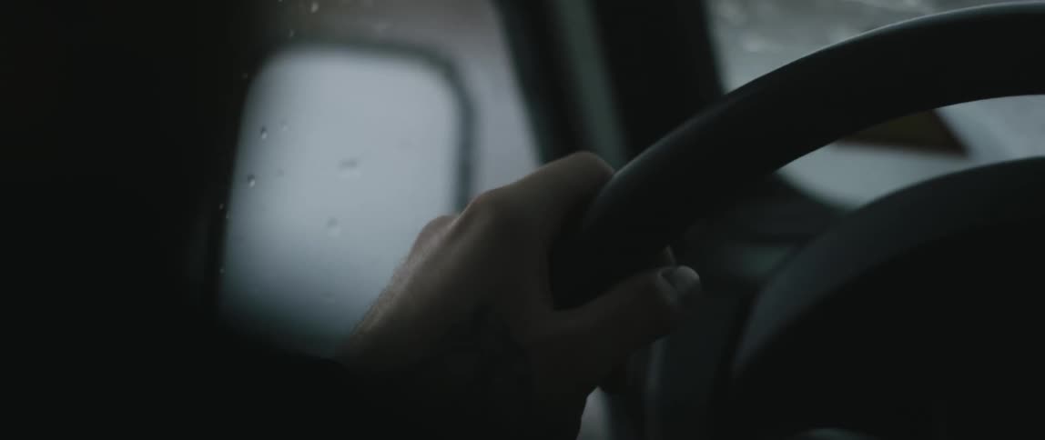 A person grips the steering wheel of their vehicle as they drive quickly along a road