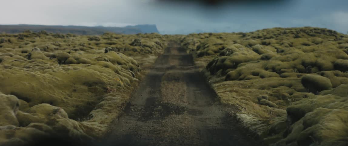 A vehicle drives down a dirt road through a canyon covered in algae