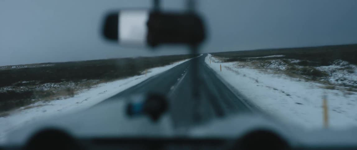 A man drives down a snowy road with his windshield wipers on