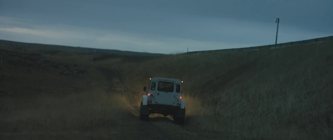 White jeep drives uphill in the field at dusk