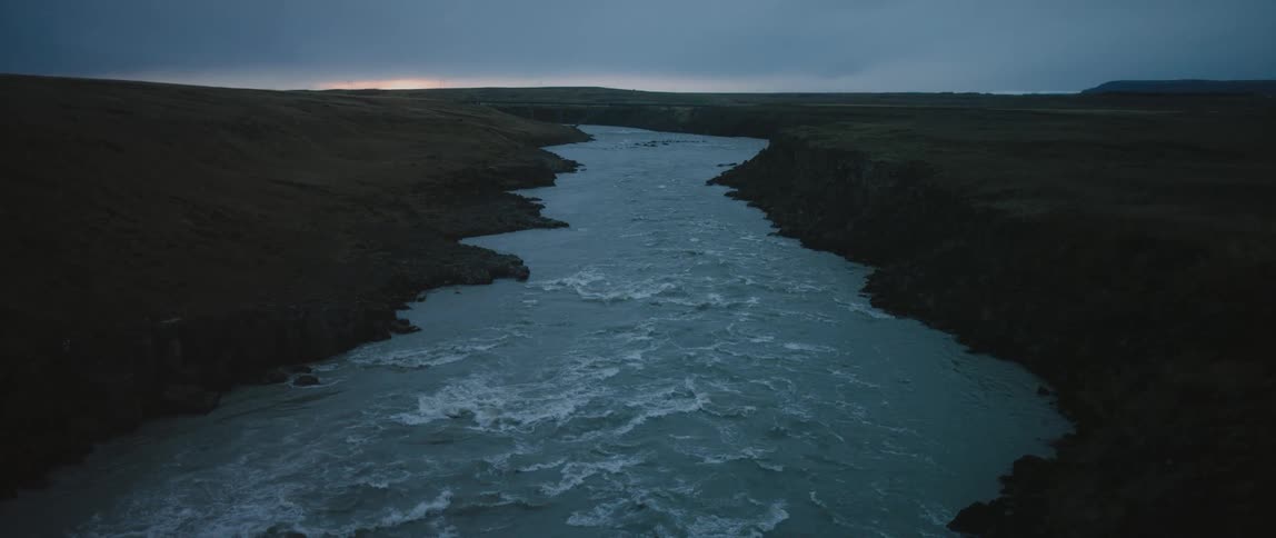 Water flows swiftly in a river while the sun hangs low in the cloudy sky