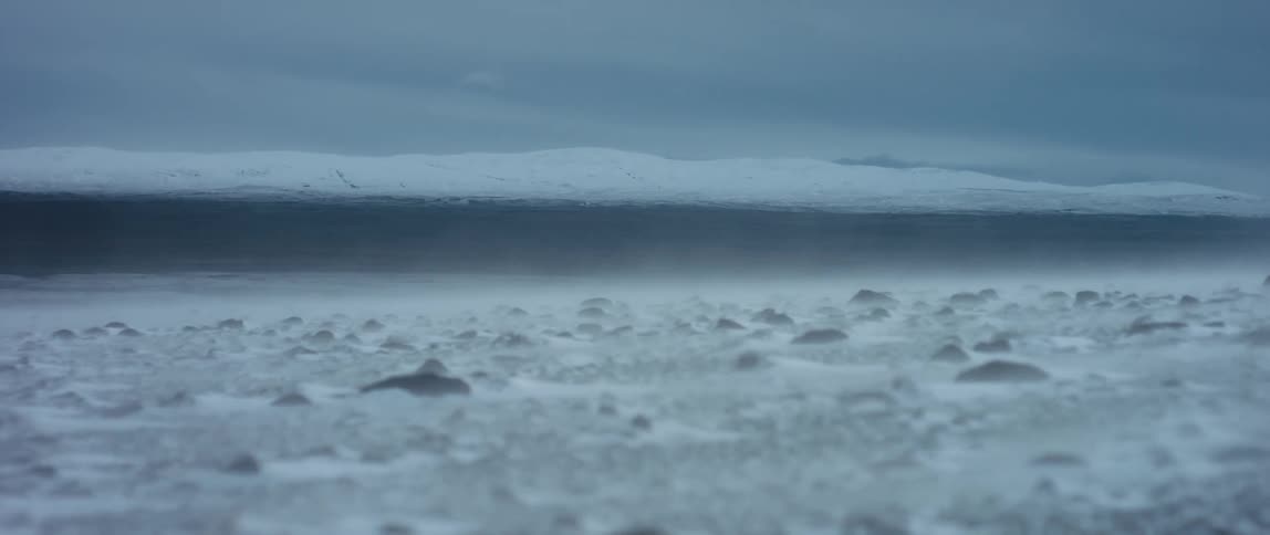 Wind blows snow across a rocky plain on a cloudy day