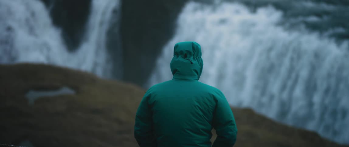 Person wearing a green hooded coat watches the waterfall