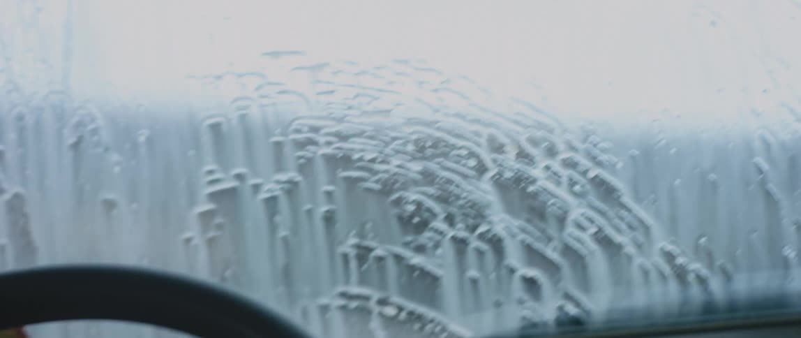 A man turns on his vehicles wipers and cleans the windshield while driving around a bend