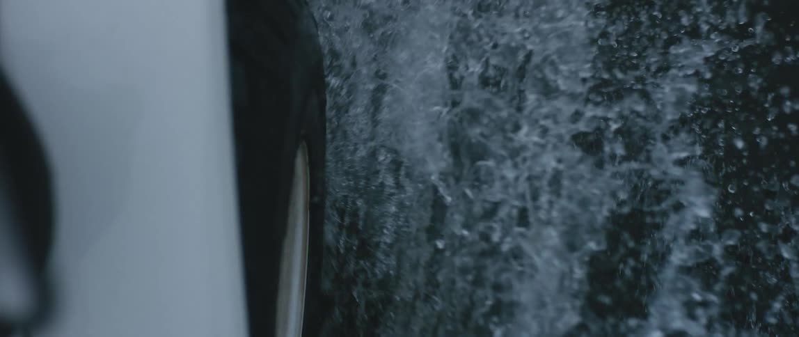 The wheel of a vehicle is seen as it drives through water and over rocky terrain