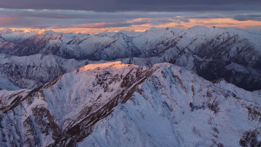 Sun shining on a few snow dusted mountain peaks in a range at sunrise