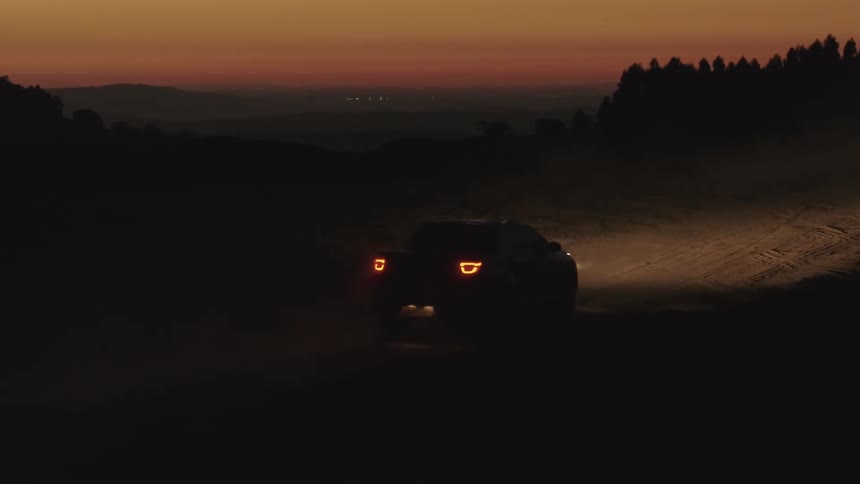 A car traveling on a sandy dirt road lit only by its headlights