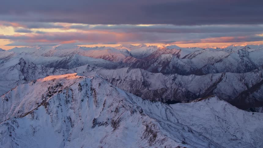 Sun colors clouds and summits of snow covered mountain range