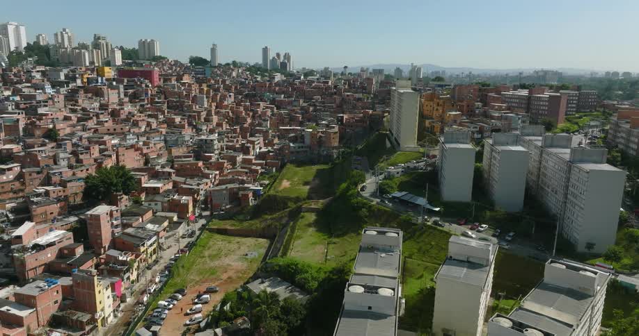 A neighborhood of crowded buildings is surrounded by towers and skyscrapers with a big city in the distance